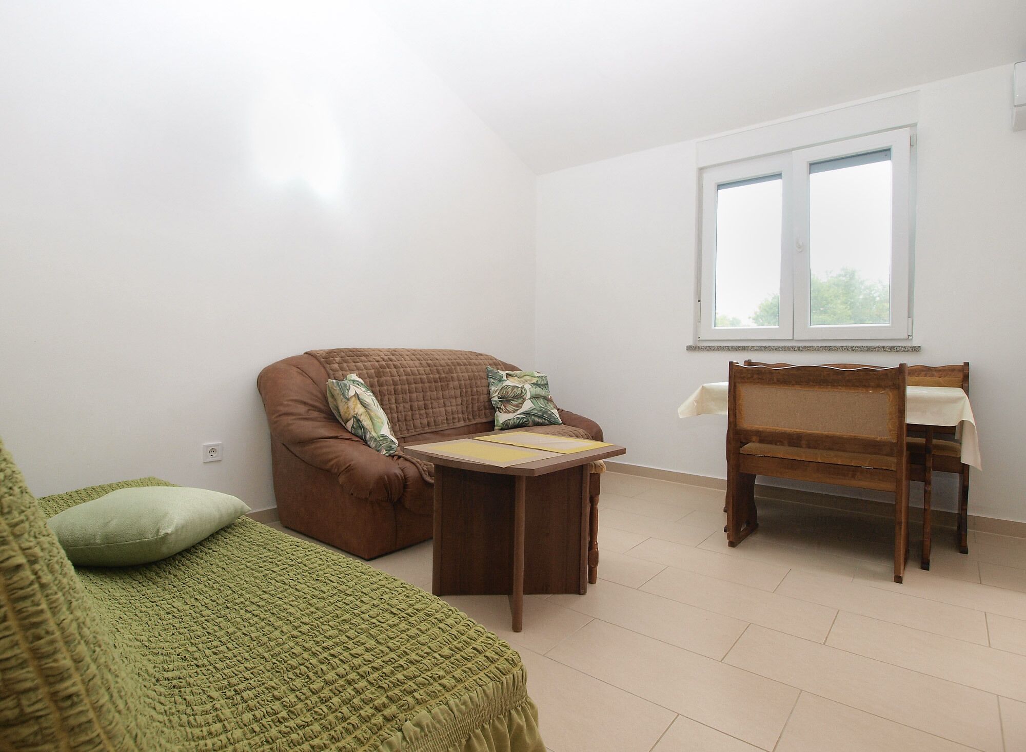 Une pièce avec un canapé marron, une couverture verte, une table en bois et une chaise en bois.