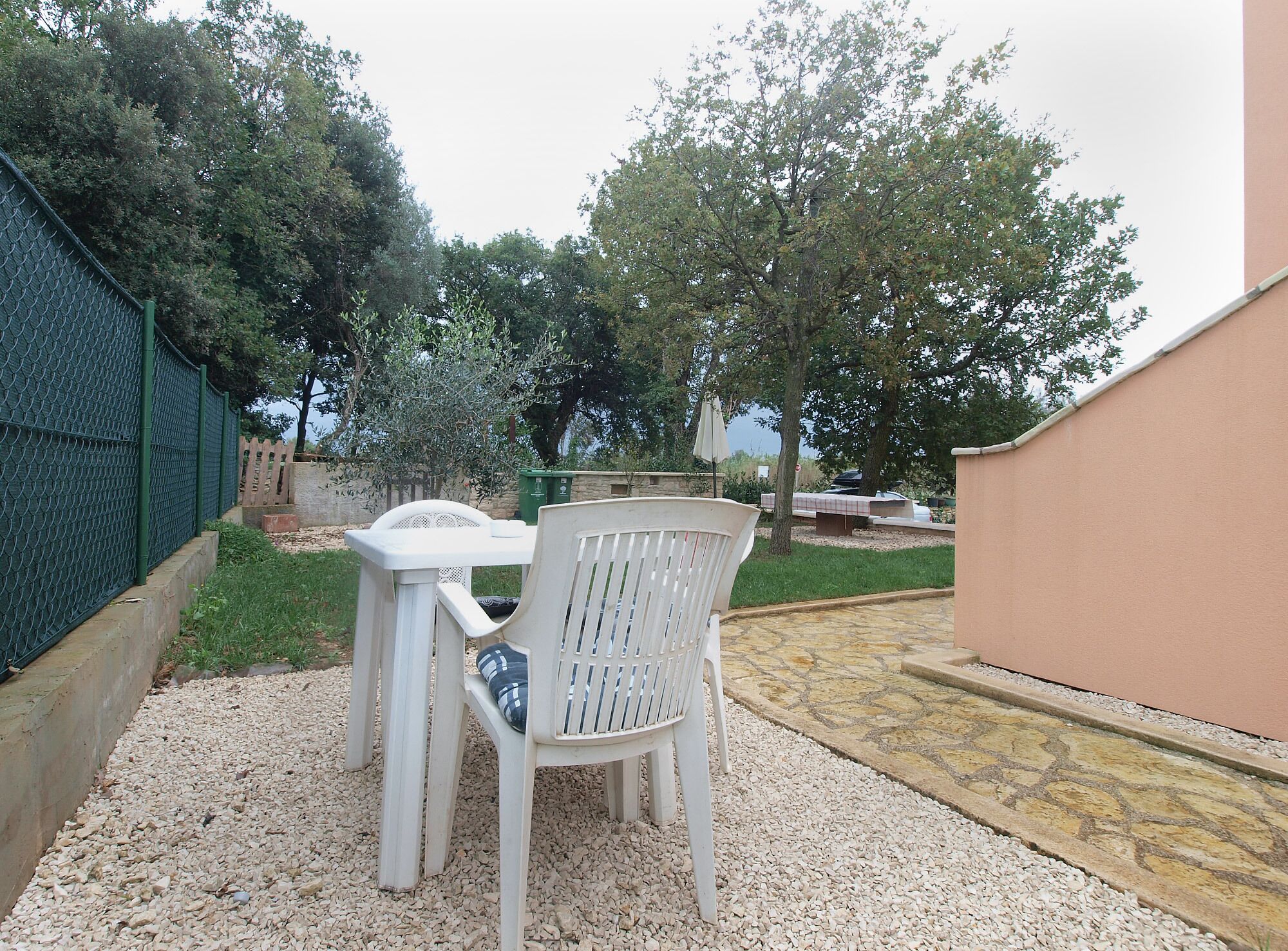A patio area with a white plastic table and chair, surrounded by gravel and greenery.