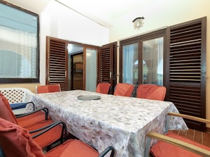 A dining area with a table covered in a patterned tablecloth, surrounded by orange chairs.