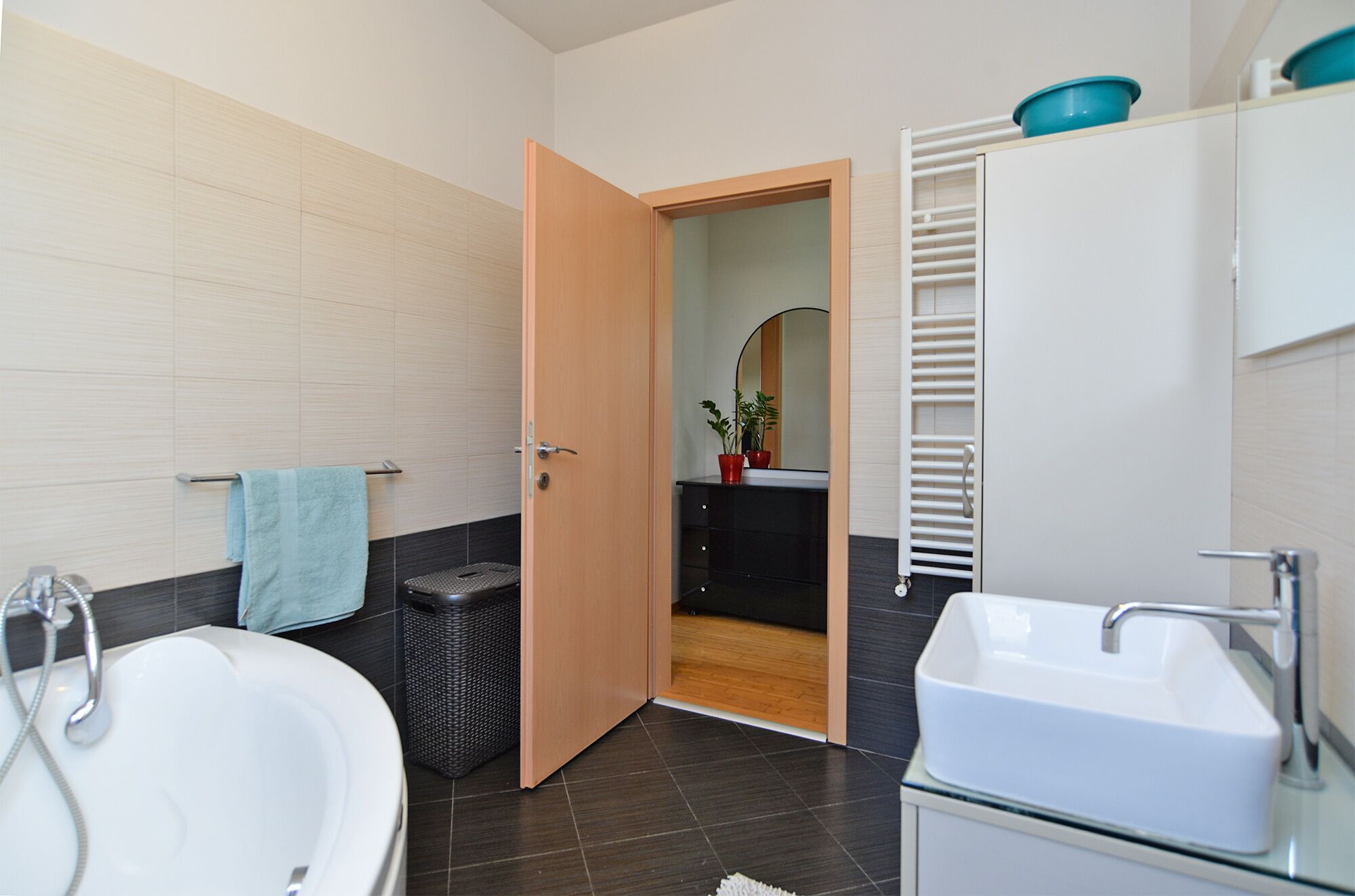 A modern bathroom with a bathtub, a sink, a shower, and a toilet. There is a towel hanging on the wall and a trash bin next to the toilet.