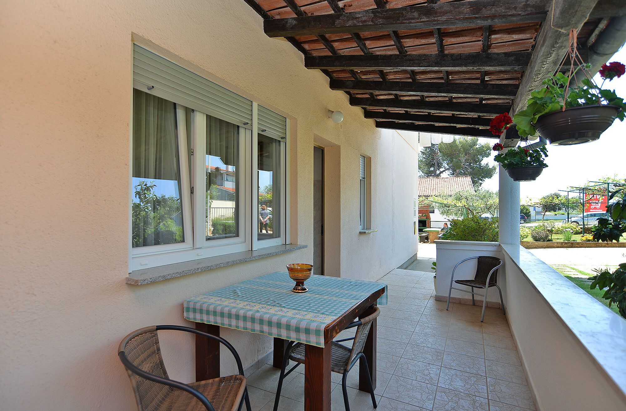 A covered patio with a table and chairs, a hanging plant, and a view of the street.