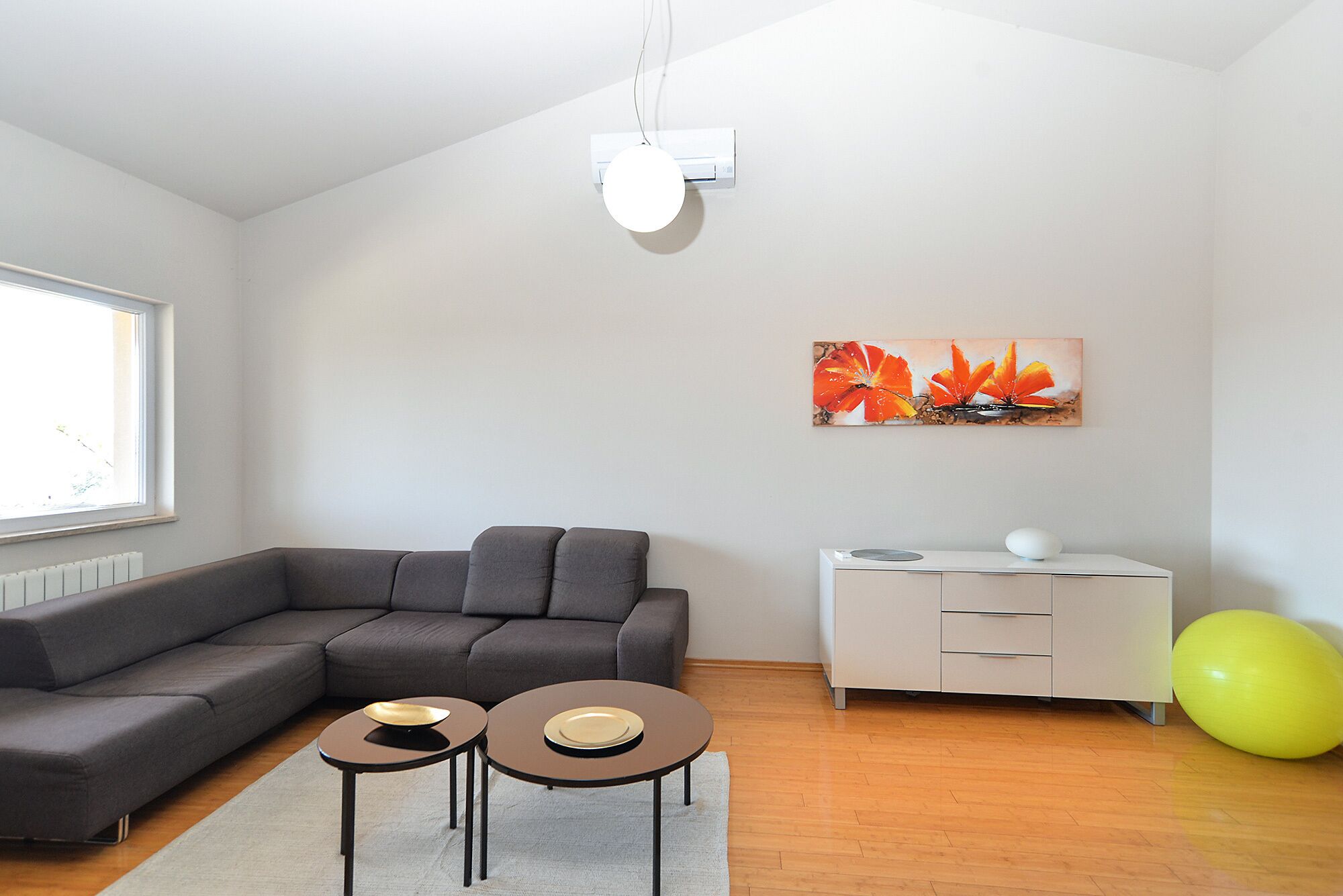 A modern living room with a grey sofa, two small tables, a white cabinet, and a painting of orange flowers.