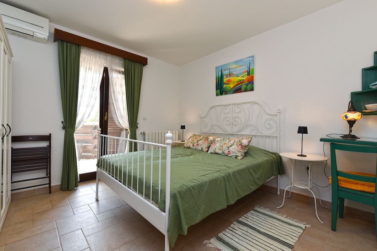 Ein Schlafzimmer mit einem Bett, einem Nachttisch, einer Lampe, einem Gemälde und einem Fenster mit Vorhängen.
