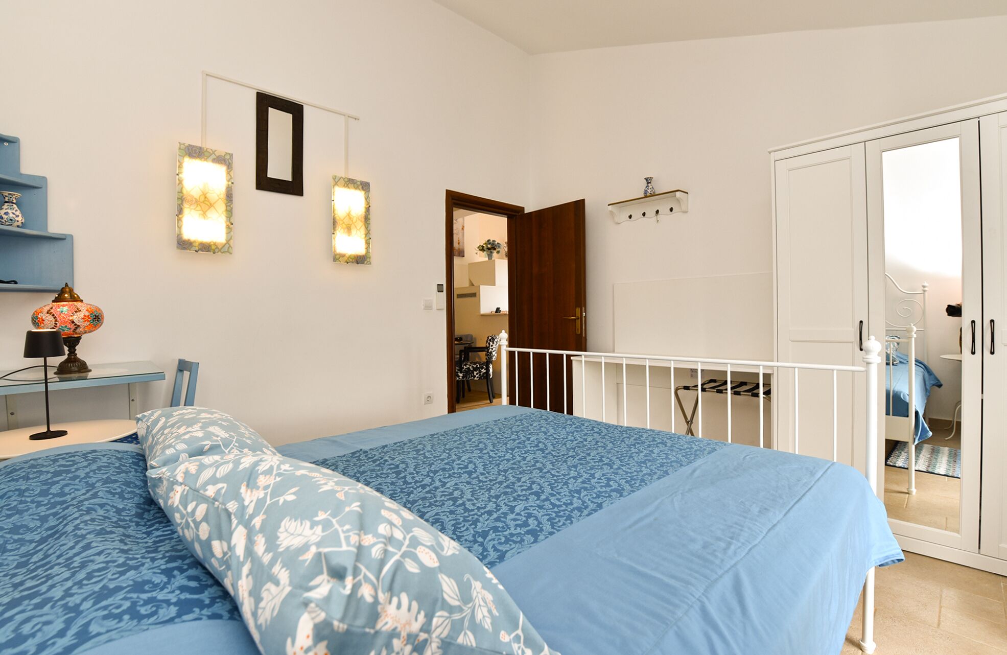 Een slaapkamer met een bed, een bureau en een stoel. Er is een deur die leidt naar een balkon.
