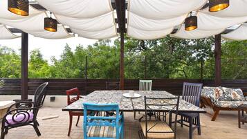 An outdoor patio with a tiled table and chairs, draped white fabric overhead, and a wooden fence in the background.