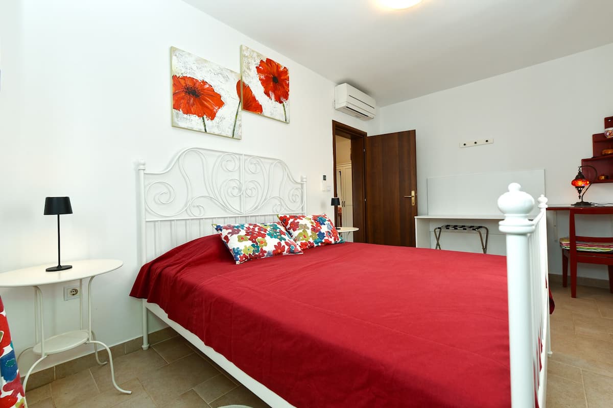 Ein Schlafzimmer mit weißem Metallbettgestell, einer roten Bettdecke und zwei an der Wand befestigten Bildern von roten Blumen.
