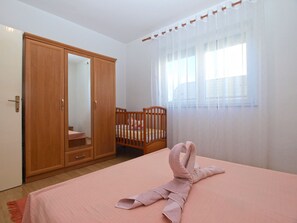 Ein Schlafzimmer mit einem Bett, einem Holzschrank, einem Babybett und einem Fenster mit durchsichtigen Vorhängen.