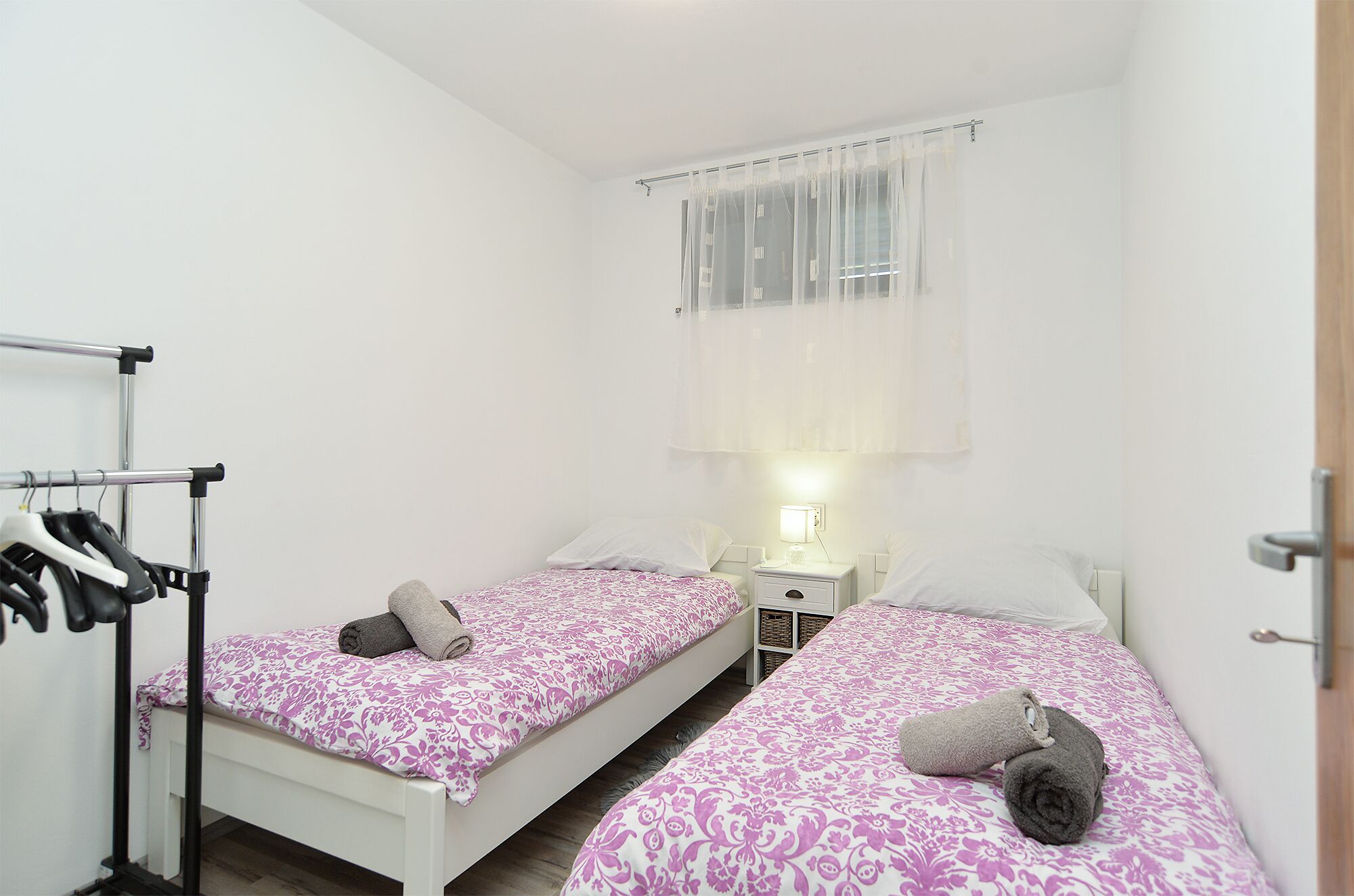 Ein kleines, sauberes Zimmer mit zwei Einzelbetten, einem Kleiderschrank und einem Nachttisch mit Lampe.