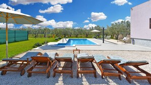 A pool area with lounge chairs and umbrellas, surrounded by a garden and a building. - House 1790 (Medulin)