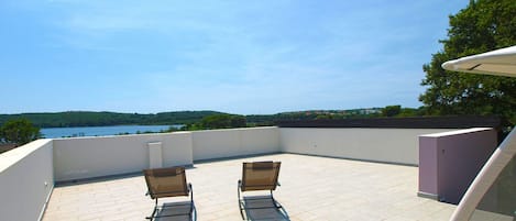 A rooftop terrace with two chairs and a table, overlooking a lake and hills.