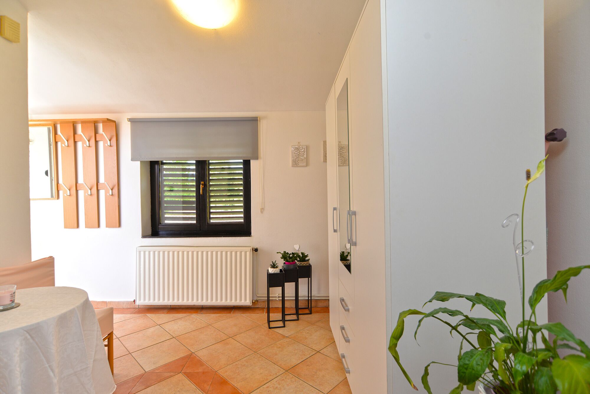 A room with a radiator, a window with blinds, a small table with a candle, and a potted plant.