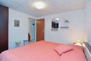 Ein Schlafzimmer mit einem Bett, einem kleinen Hocker, einem Spiegel und einem Regal mit einer Pflanze.