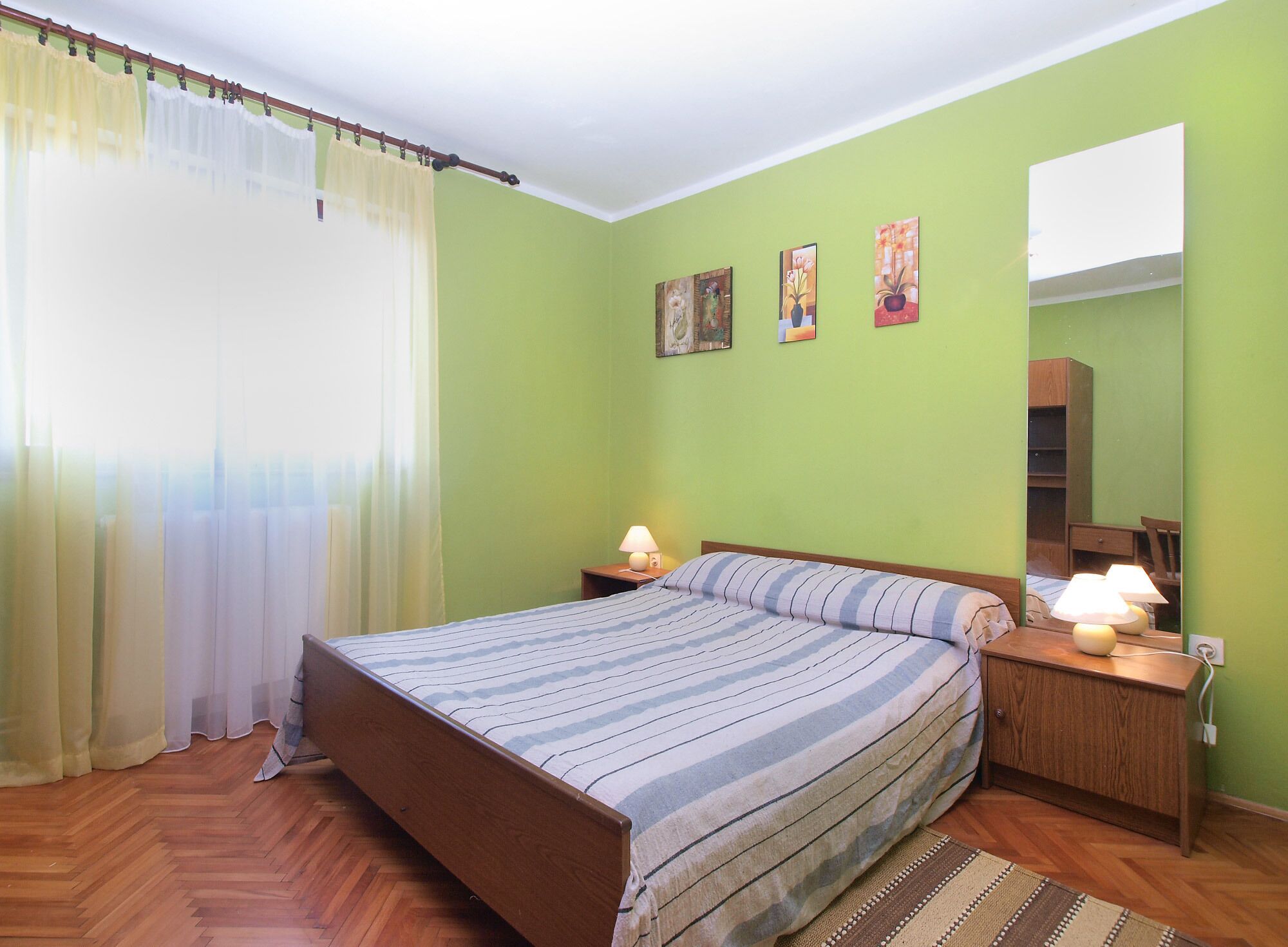 A bedroom with a bed, two nightstands, a mirror, and a window with curtains.