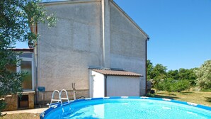 An outdoor swimming pool with a ladder, surrounded by a stone wall and a grassy area. - Apartment 1794 (Liznjan)