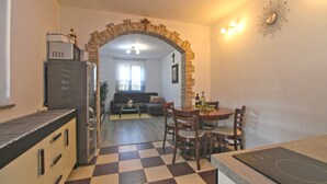 Una cocina con piso a cuadros, una zona de comedor con mesa y sillas, y una sala de estar con sofá y televisor.