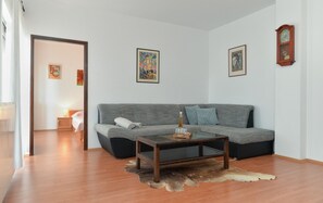A living room with a grey sofa, a glass coffee table, and a fur rug. There are two framed artworks on the wall and a wooden clock. - Apartment 1803 (Vodnjan)
