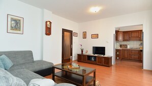 A living room with a grey sofa, a coffee table, a television, and a kitchen area with wooden cabinets. - Apartment 1803 (Vodnjan)