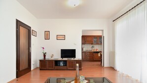 A living room with a glass coffee table, wooden cabinets, a flat-screen TV, and a kitchen in the background. - Apartment 1803 (Vodnjan)