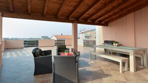 An outdoor patio with wicker furniture, a wooden table, and a barbecue grill. - Apartment 1803 (Vodnjan)