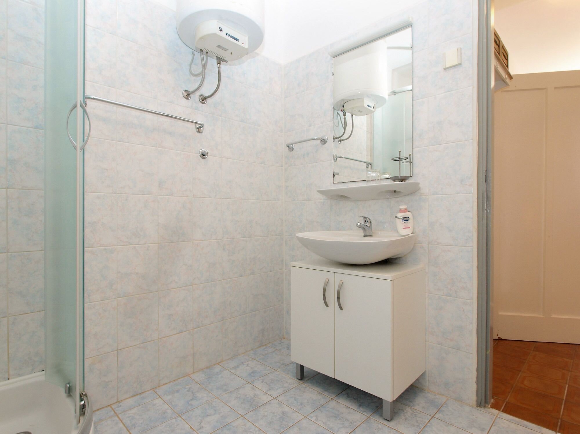 A bathroom with a glass shower enclosure, a white sink with a mirror above it, and a cabinet below.