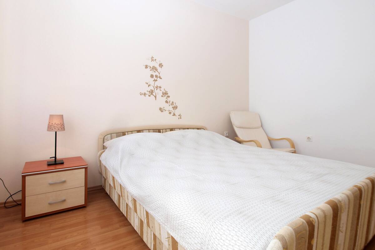 A bedroom with a bed, a bedside table, a lamp, and a chair.