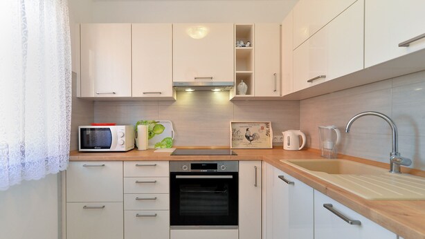 Una cocina moderna con armarios blancos, un microondas, una tetera y un lavabo.