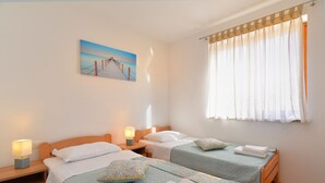 Habitación de hotel con dos camas individuales, una mesita de noche con lámpara, un cuadro en la pared y una ventana con cortinas.