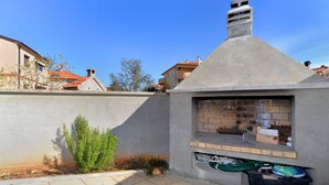 Un espacio exterior de hormigón con un horno de ladrillo, una planta pequeña y una manguera.