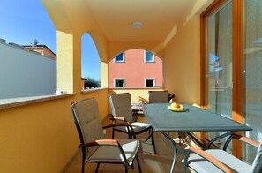 Een balkon met een tafel en stoelen, een uitzicht op een gebouw, en een raam met gordijnen.