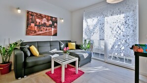 Ein modernes Wohnzimmer mit einer schwarzen Couch, einem weißen Couchtisch und einem großen Fenster mit gemusterten Vorhängen.