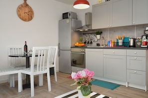 Une cuisine moderne avec des meubles gris, un réfrigérateur en acier inoxydable et un coin repas comprenant une table et des chaises blanches.