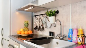 Eine moderne Küche mit einem Edelstahlspülbecken, einem eingebauten Herd und einer Dunstabzugshaube. Küchenutensilien hängen an der Wand und ein Blumentopf steht dort.