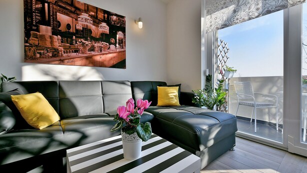 Ein modernes Wohnzimmer mit einem schwarzen Ledersofa, einem gestreiften Couchtisch und einem großen Fenster mit Blick ins Freie.
