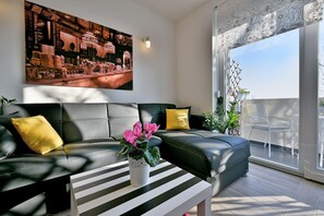 A modern living room with a black leather sofa, a striped coffee table, and a large window with a view of the outdoors. - Apartment 1811 (Rijeka)