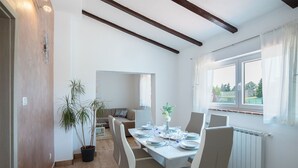 A dining area with a long table set for four, a potted plant, and a view of the outdoors through a window. - Apartment 1816 (Barban)