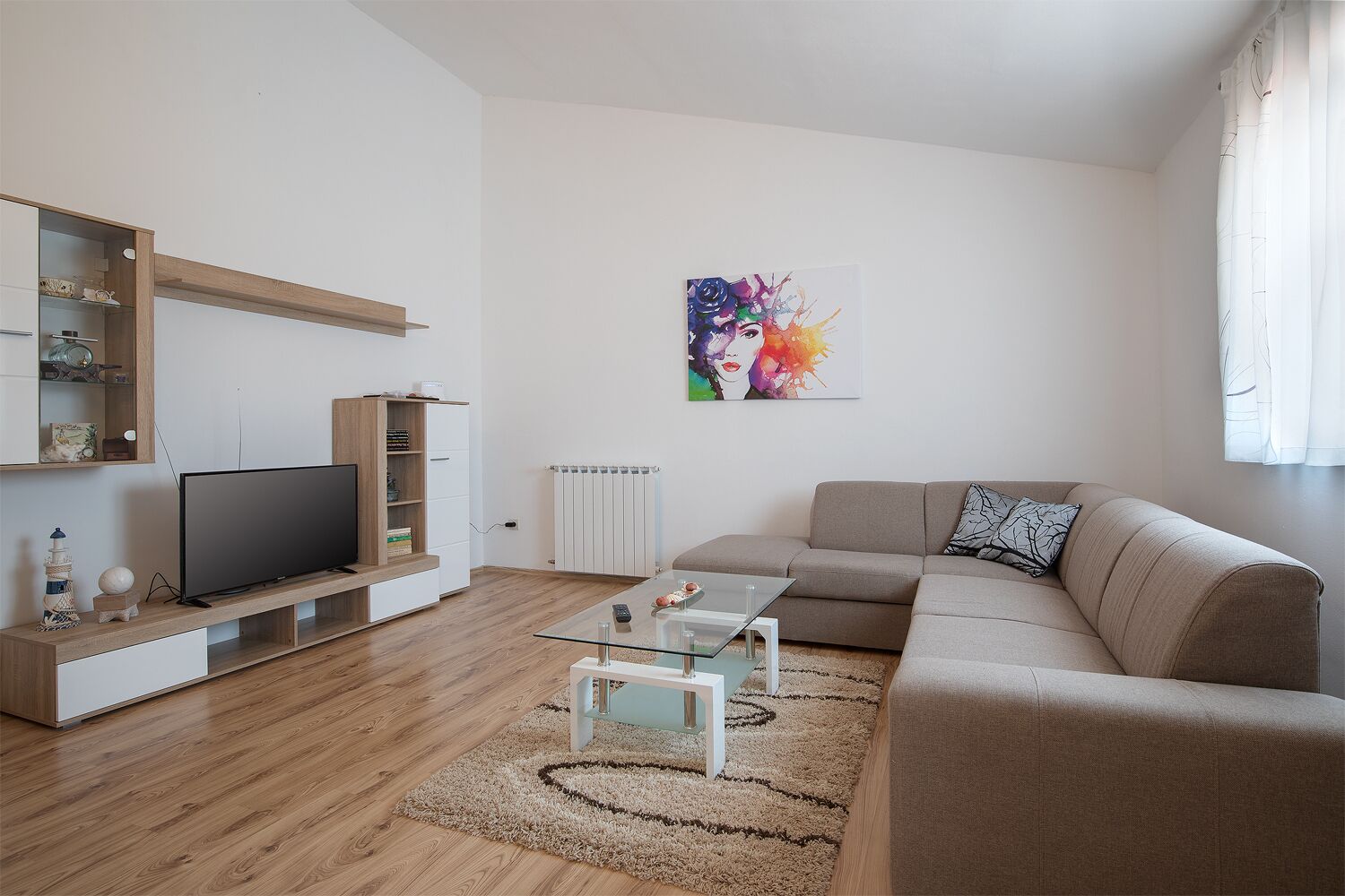 A modern living room with a flat-screen TV, a sofa, a glass coffee table, and a colorful abstract painting on the wall.