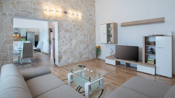 A modern living room with a stone accent wall, a flat-screen TV, and a minimalist entertainment unit. - Apartment 1816 (Barban)