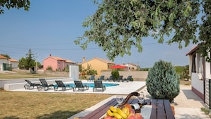 A poolside area with lounge chairs, a table with fruit, and a view of houses and greenery. - Apartment 1816 (Barban)
