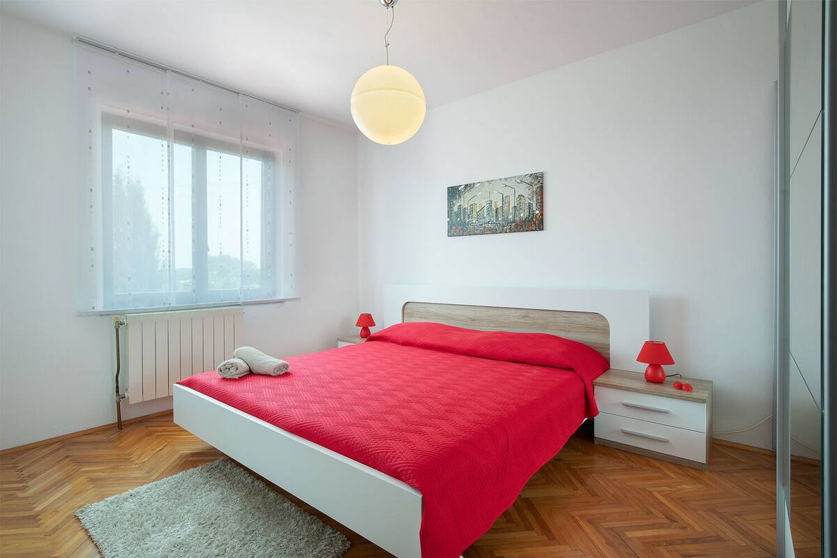 A bedroom with a bed, bedside tables, a window, and a painting on the wall.