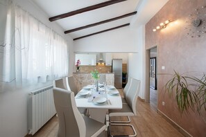 A modern dining area with a long table set for four, a kitchen in the background, and a decorative wall piece. - Apartment 1816 (Barban)