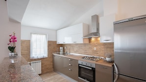 A modern kitchen with a built-in oven, a stainless steel refrigerator, and a window with sheer curtains. - Apartment 1816 (Barban)