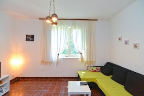 Ein Wohnzimmer mit einer Couch, einem kleinen Tisch, einer Lampe und einem Fenster mit Vorhängen.