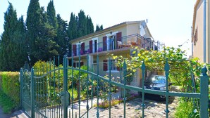 A two-story house with a balcony, surrounded by a garden and a metal fence. - Apartment 1817 (Fazana)