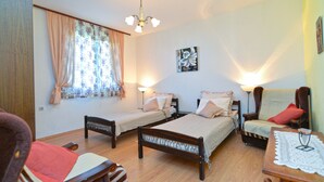 A room with two single beds, a wooden floor, a window with floral curtains, a wall-mounted picture, and two bedside lamps. - Apartment 1817 (Fazana)