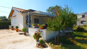 Une maison avec un toit en tuiles, un balcon orné de plantes en pot et un petit arbre dans le jardin.