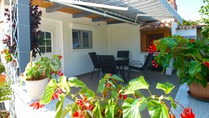 Une terrasse extérieure avec un auvent rayé, une table et des chaises, ainsi que des plantes en pot.