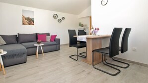 Un salon moderne avec un canapé gris, une petite table ronde et une table à manger en bois, accompagnée de chaises.