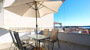 Een balkon buiten met een tafel, stoelen, een grote parasol en uitzicht op een kustplaats.