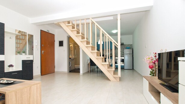 Een modern appartement met een houten trap, een keuken en een woonruimte met een televisie en een houten salontafel.
