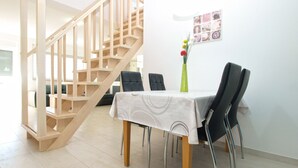 Een eetruimte met een houten trap, een tafel met stoelen en een vaas met bloemen.